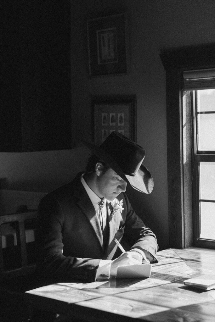 Black and white photograph of a groom in a cowboy hat signing a note to the bride at The Gage Hotel in Marathon, Texas. 